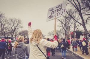 A group of protestors, with one carrying a sign that says 'We Are Better Than This.'