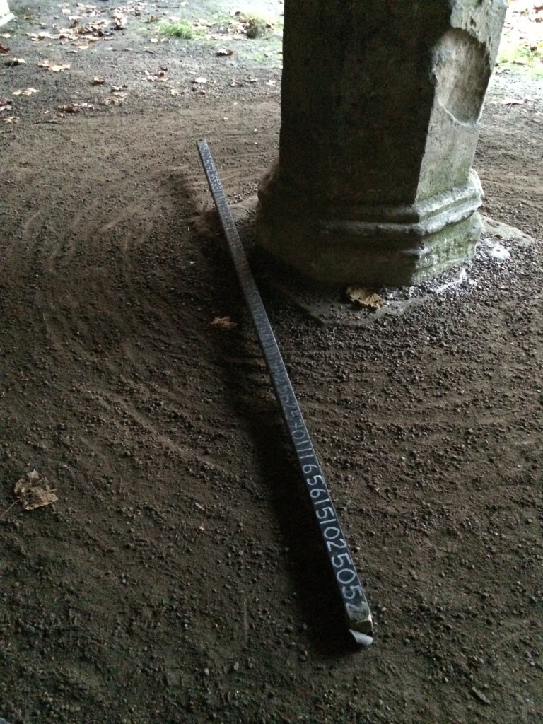  Image of the ground, one arch in view, and one of the planks inscribed with numbers lies on the floor.